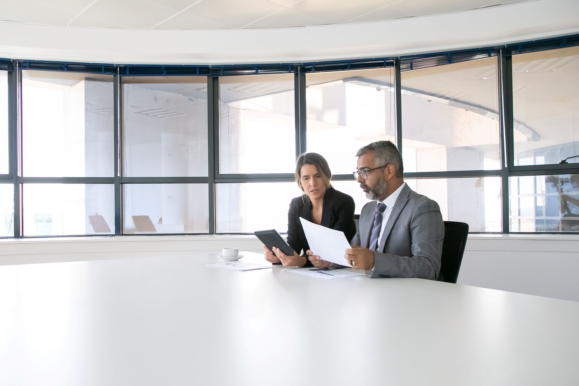 company-executives-analyzing-discussing-reports-two-business-colleagues-sitting-together-looking-document-holding-tablet-talking-wide-shot-communication-concept